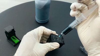 Persona con guantes rellenando un cartucho de tinta con una jeringuilla