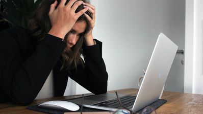 Mujer con las manos en la cabeza delante de un portátil