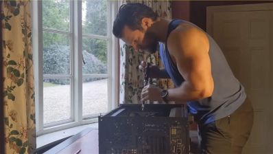 Henry Cavill concentrado montando los componentes internos de su ordenador personal junto a una ventana.