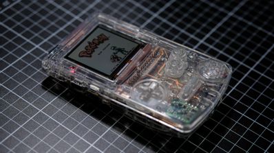 Prototipo funcional de Game Boy Color con carcasa y PCB transparentes, mostrando los componentes internos iluminados mientras ejecuta un juego.