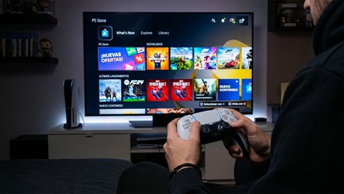 Persona sentada frente a un televisor que muestra la interfaz de PlayStation Store mientras sujeta un mando DualSense.