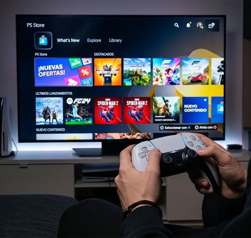 Persona sentada frente a un televisor que muestra la interfaz de PlayStation Store mientras sujeta un mando DualSense.