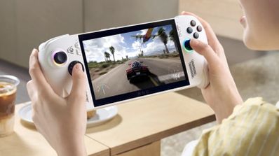 Primer plano de una persona sujetando una consola portátil ASUS ROG Ally blanca mientras juega a un videojuego de carreras en una mesa.