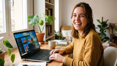 Mujer joven sonriendo mientras trabaja con un ordenador portátil que muestra la interfaz de Windows 10 en un escritorio de madera.