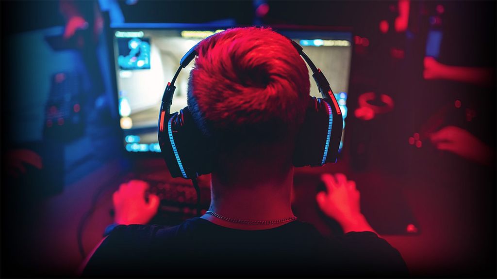 Persona de espaldas jugando a videojuegos con auriculares de diadema en una habitación iluminada con luces rojas y azules.