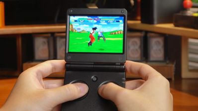 Manos sosteniendo una consola portátil Anbernic RG SP de diseño plegable mientras ejecuta un videojuego de lucha en 2D.