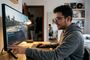 Joven con gafas configurando un monitor gaming de pantalla ancha mientras juega a un simulador de conducción en su escritorio.