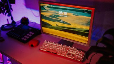 Monitor de ordenador antiguo con pantalla de bloqueo moderna junto a un teclado mecánico retroiluminado en un escritorio con iluminación ambiental morada.
