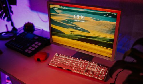 Monitor de ordenador antiguo con pantalla de bloqueo moderna junto a un teclado mecánico retroiluminado en un escritorio con iluminación ambiental morada.