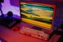 Monitor de ordenador antiguo con pantalla de bloqueo moderna junto a un teclado mecánico retroiluminado en un escritorio con iluminación ambiental morada.