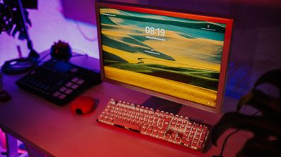 Monitor de ordenador antiguo con pantalla de bloqueo moderna junto a un teclado mecánico retroiluminado en un escritorio con iluminación ambiental morada.