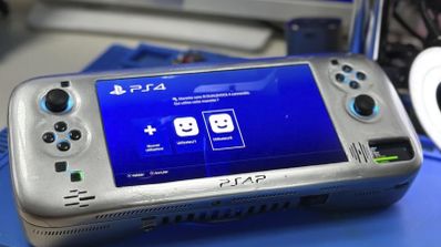 Consola portátil personalizada con carcasa metálica plateada mostrando la interfaz de usuario de PlayStation 4 en su pantalla central.