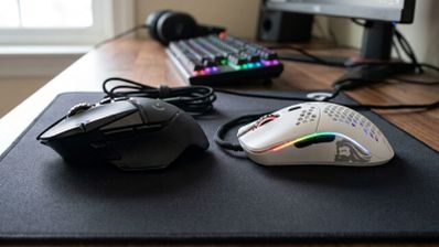 Comparativa entre un ratón gaming ergonómico negro de perfil robusto y un ratón ultraligero blanco con diseño de panal sobre una alfombrilla.