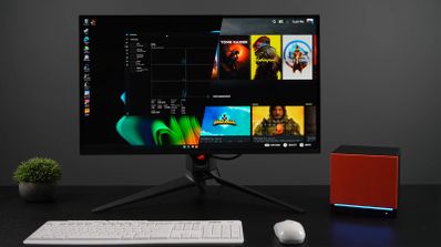 Monitor de diseño mostrando una interfaz de biblioteca de videojuegos dividida temáticamente junto a una mini PC de color naranja y negro.