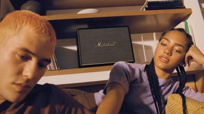 Altavoz Marshall Woburn ubicado en una estantería de madera entre dos personas jóvenes en un ambiente doméstico.