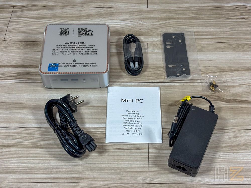 Contenido de la caja del mini PC NiPoGi P2 con cables, manual y accesorios sobre una mesa de madera.