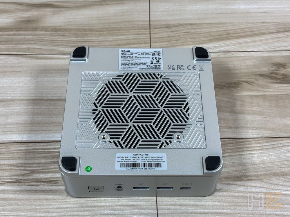 Parte inferior del mini PC NiPoGi P2 que muestra la rejilla de ventilación con patrón geométrico y patas de goma antideslizantes sobre una superficie de madera.