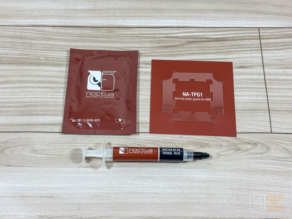 Kit de pasta térmica Noctua compuesto por jeringa aplicadora, toallita de limpieza y protector para procesadores AM5 sobre una superficie de madera.