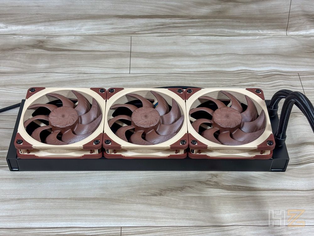 Tres ventiladores marrones y crema instalados en un radiador negro sobre una superficie de madera.