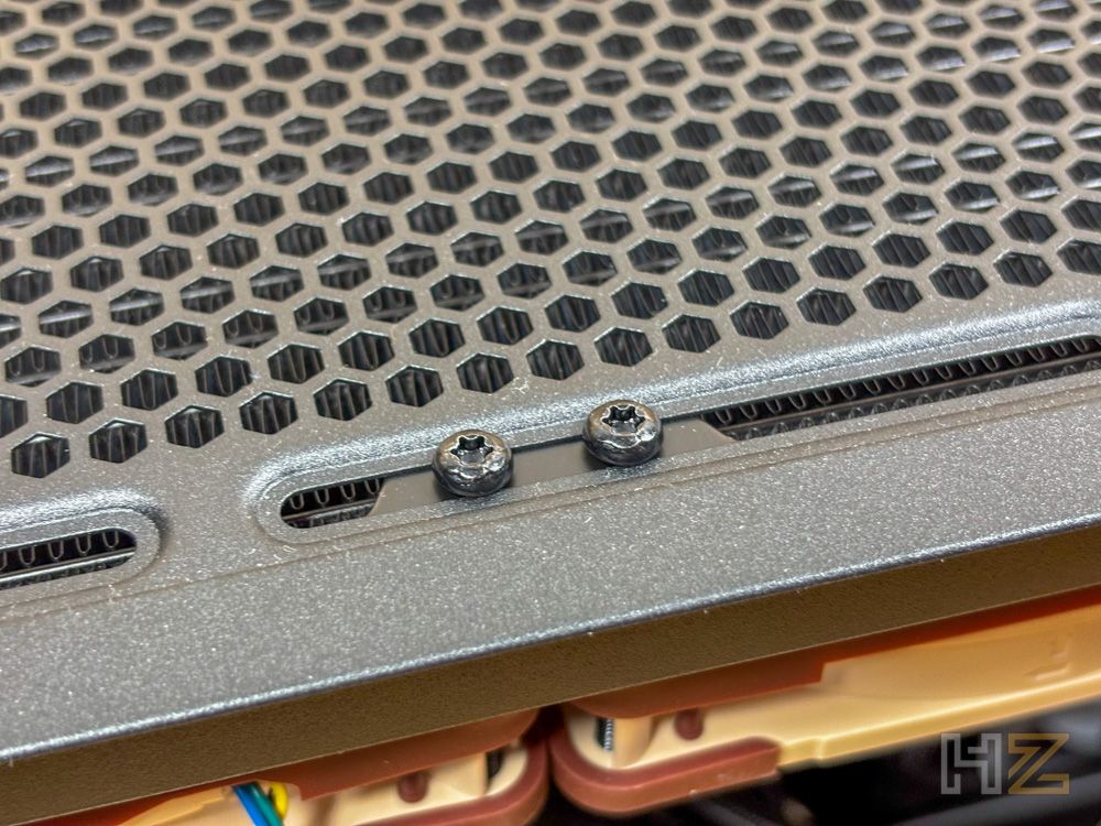 Detalle de dos tornillos de fijación instalados en el carril de montaje de una caja de ordenador con rejilla hexagonal.