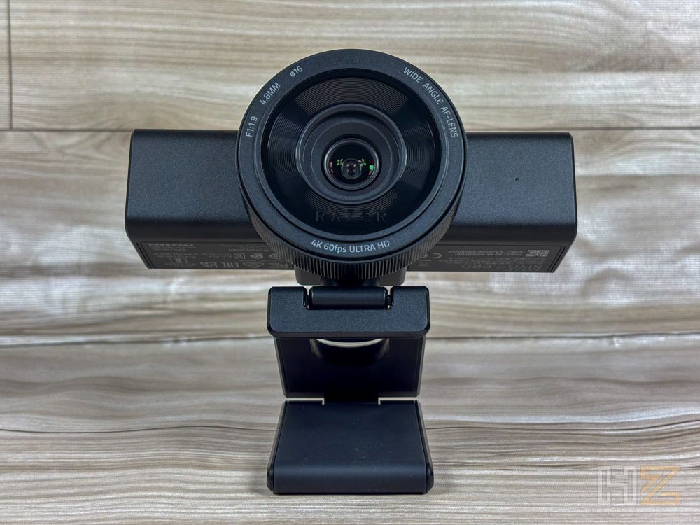 Primer plano frontal de la webcam Razer Kiyo V2 Pro sobre su soporte plegable en una superficie de madera.