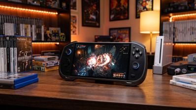 Consola portátil ARC-X1 ejecutando un juego de acción sobre un escritorio de madera rodeado de juegos y consolas clásicas.