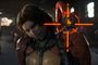 Primer plano de un personaje femenino con armadura y una mira naranja sobre su hombro en Death Stranding 2.