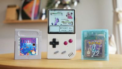 Consola FPGB Mini encendida mostrando un combate de Pokémon junto a cartuchos originales de Tetris y Pokémon Cristal.