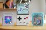 Consola FPGB Mini encendida mostrando un combate de Pokémon junto a cartuchos originales de Tetris y Pokémon Cristal.