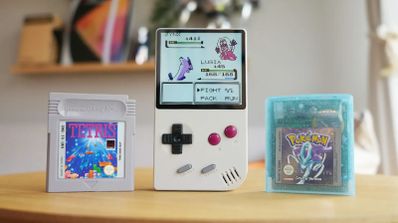 Consola FPGB Mini encendida mostrando un combate de Pokémon junto a cartuchos originales de Tetris y Pokémon Cristal.