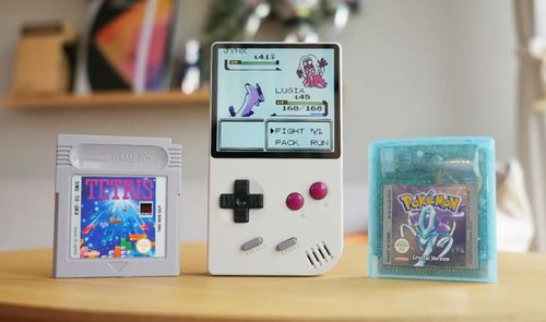 Consola FPGB Mini encendida mostrando un combate de Pokémon junto a cartuchos originales de Tetris y Pokémon Cristal.