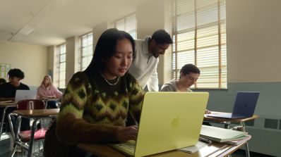 Estudiante en un aula utilizando un MacBook Neo de color amarillo mientras sus compañeros trabajan en segundo plano.