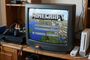 Menú principal de Minecraft ejecutándose en un televisor de tubo antiguo rodeado de una PlayStation 2 y una Nintendo Wii.