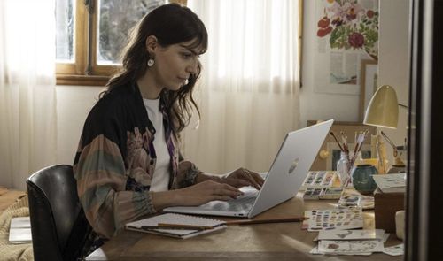 Una mujer trabajando con un portátil HP de color plata en un escritorio junto a una ventana.