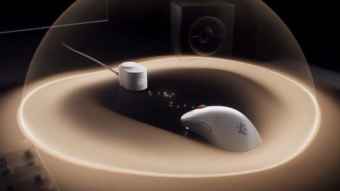 Ratón inalámbrico SteelSeries de color blanco junto a su receptor en una superficie iluminada por una cúpula de luz.