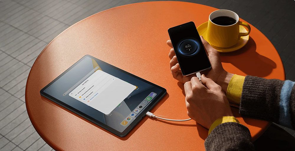 Conexión de cable USB entre una tablet POCO Pad y un smartphone sobre una mesa naranja.