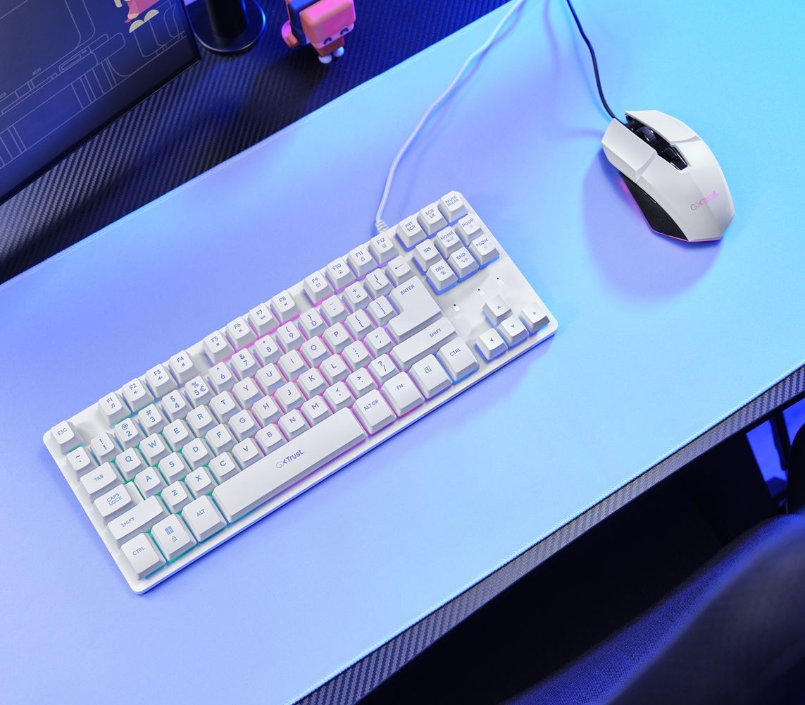 Teclado compacto de color blanco con iluminación sutil sobre una alfombrilla azul junto a un ratón a juego.