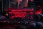 Teclado mecánico 8bitdo con retroiluminación roja intensa inspirado en Gears of War E-Day sobre un fondo de ciudad en ruinas.