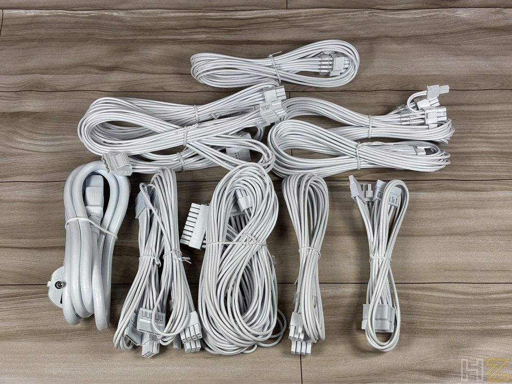 Conjunto de cables modulares de color blanco pertenecientes a la fuente de alimentación Corsair RM1200e desplegados sobre una superficie de madera.