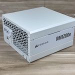 Fuente de alimentación Corsair RM1200e blanca vista en perspectiva sobre una superficie de madera.