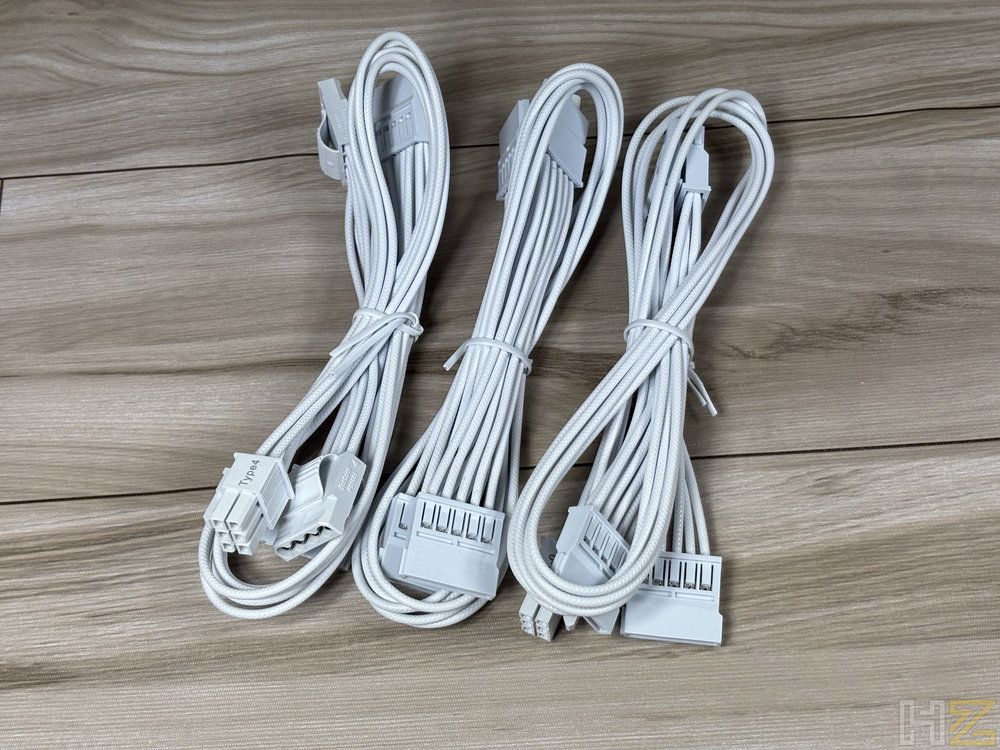 Tres mazos de cables modulares de color blanco con conectores negros sobre una superficie de madera.