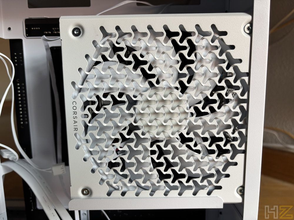 Primer plano de la rejilla de ventilación blanca con patrón triangular de la fuente de alimentación Corsair RM1200e instalada en un chasis.