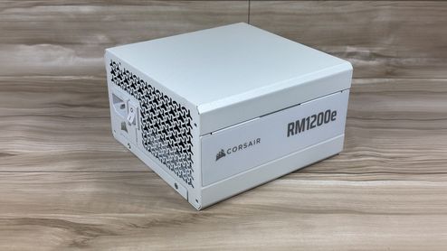 Fuente de alimentación Corsair RM1200e blanca vista en perspectiva sobre una superficie de madera.
