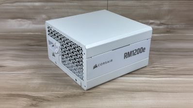 Fuente de alimentación Corsair RM1200e blanca vista en perspectiva sobre una superficie de madera.