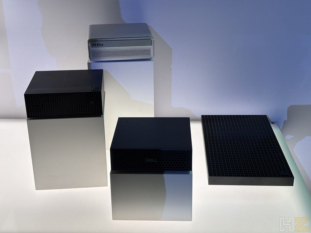 Tres ordenadores de formato pequeño sobre pedestales blancos en una exposición técnica.