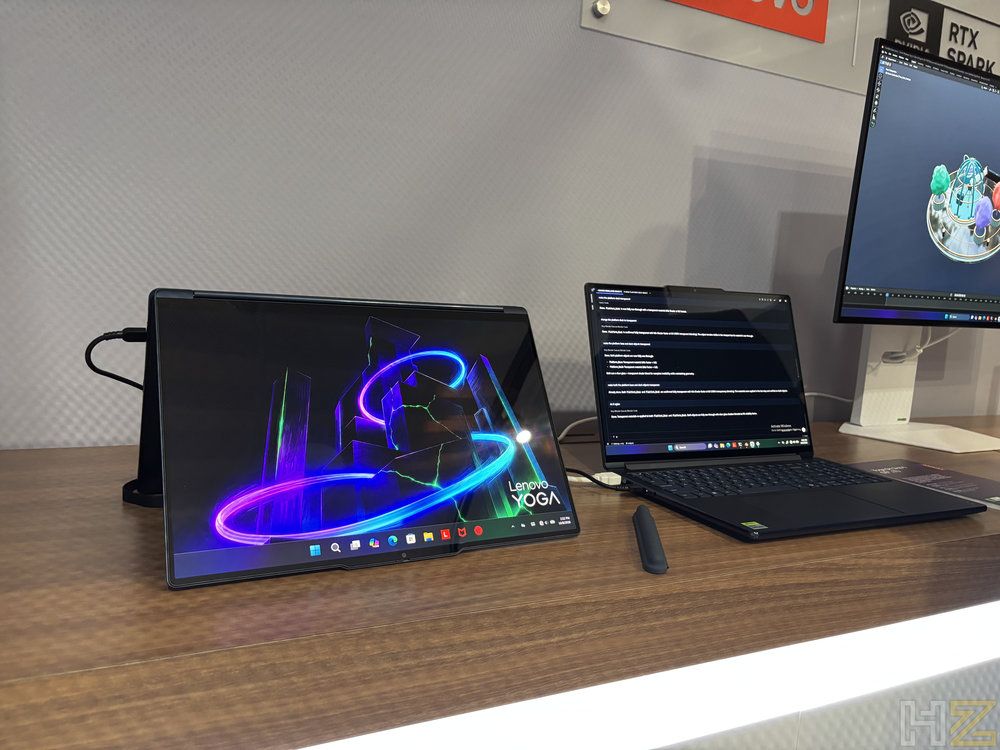 Tableta Lenovo Yoga con pantalla encendida junto a un ordenador portátil y un monitor externo en un evento de tecnología.