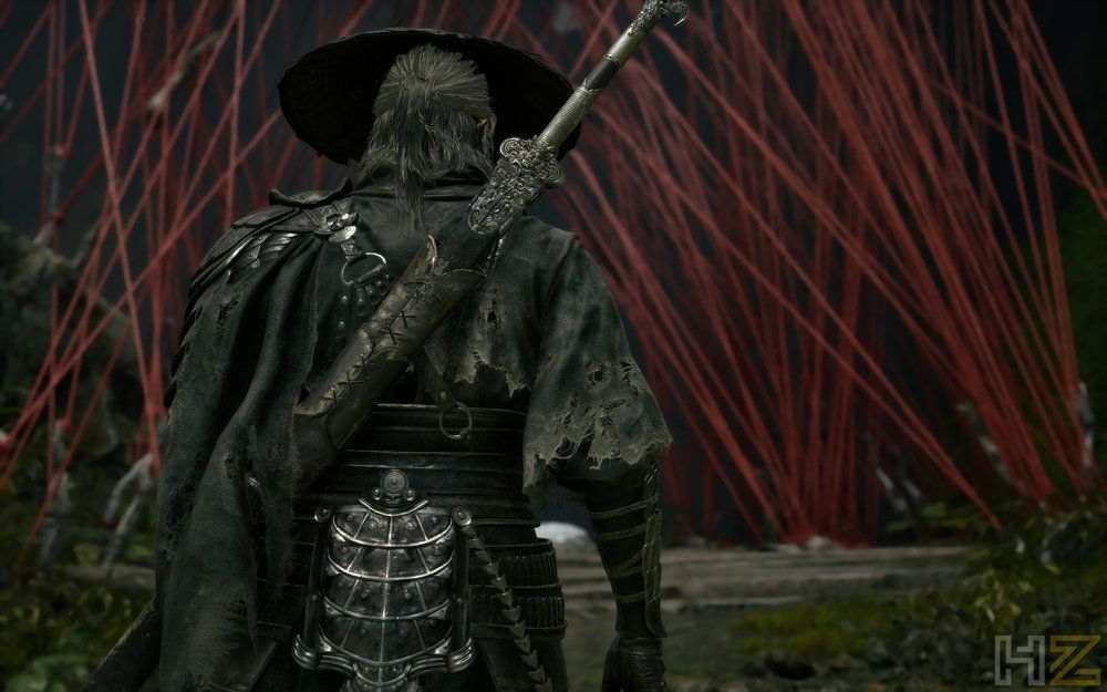 Vista de espaldas de un guerrero con sombrero y espada frente a una estructura de hilos rojos en Phantom Blade Zero.