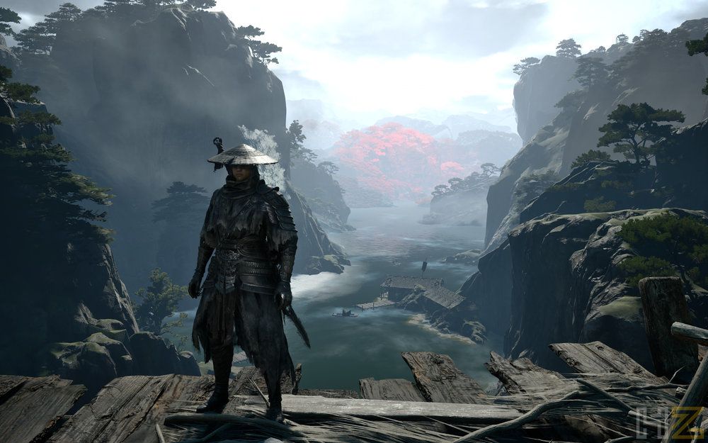 Personaje con armadura oscura y sombrero tradicional frente a un paisaje de montañas escarpadas y un río en Phantom Blade Zero.