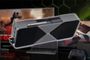 Renderización de una tarjeta gráfica RTX 5090 en primer plano sobre un fondo de salón con monitor de videojuegos y mando.