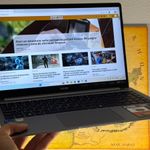 Ordenador portátil TECNO MEGABOOK T15RA sostenido con una mano mostrando una página web de noticias en pantalla.